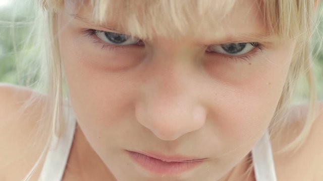 Angry frowning young girl with blond hair looking at camera close up face