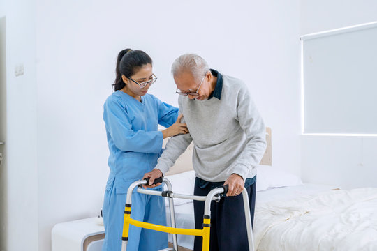 Beautiful nurse helping old man to walk in bedroom