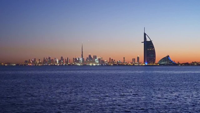 Burj Al Arab in Jumeirah Island or boat building with waves on sea beach, Dubai Downtown skyline, United Arab Emirates or UAE. Financial district in urban city. Skyscrapers at sunset.