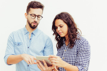 Focused couple with tablet analyzing family budget. Young woman in casual and man in glasses in glasses posing isolated over white background. Personal finance app concept