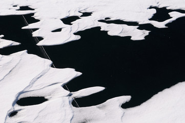 Snow drift patterns on black ice on a lake with a large deep crack