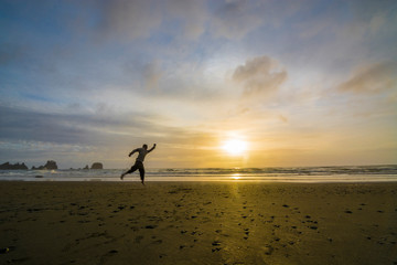 Fototapeta na wymiar Adventurous man jumping on a rugged Pacific Northwest beach during sunset.