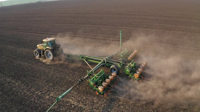 Spring field work, a tractor with a mounted seeder sow seeds in the ground on an agricultural field. aerial video