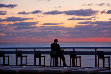 man working on computer outside by beach