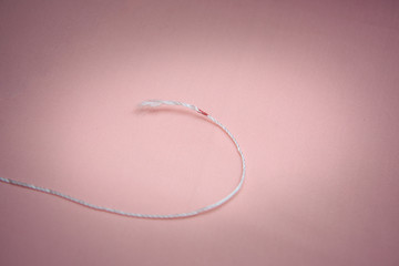White cord with a red tag on a pink background.