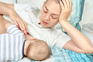 Obraz na płótnie Canvas Young mother breastfeeds her baby, lying on bed and touching him hands. Mothers day concept. Maternity and healthy lifestyle. Lactation infant concept.