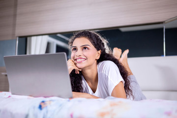 Cheerful woman daydreaming with laptop on bed