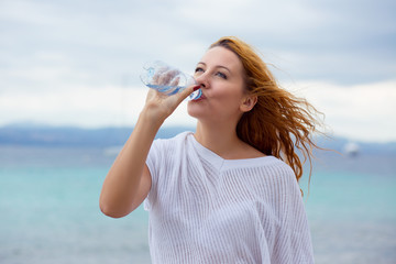 beautiful young woman drinking water in summer beach outdoor with sea background
