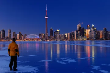 Fotobehang Man standing on frozen Lake Ontario watching Toronto city skyline light up at dusk © Reimar