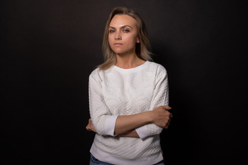 Woman standing with arm crossed seriously looks at camera. Black background