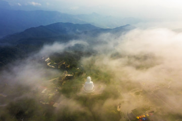 Fototapeta premium Aerial view of Linh Ung Pagoda with a giant buddha statue among green trees and sea clouds floating on the top of Ba Na mountain. Near Golden bridge. Da Nang, Vietnam