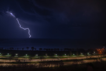 A bright bolt of lightning shoots out of a thunderstorm cloud as the storm moves over Lake Michigan and cars pass by on Lake Shore Drive on Chicago's north side at night.