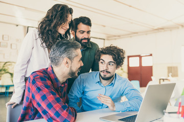 Obraz premium Positive coworkers in casual sharing ideas for project at laptop. Business colleagues in casual meeting in contemporary office space. Brainstorming concept