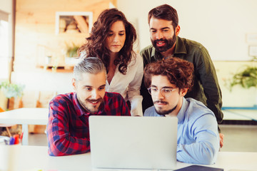 Excited coworkers in casual looking at laptop monitor, watching content. Business colleagues in casual meeting in contemporary office space. Teamwork concept