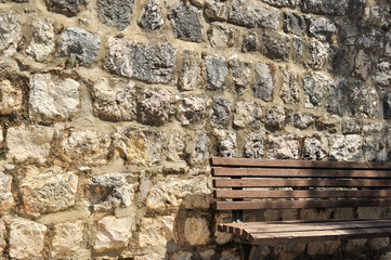 Wooden street bench against an old stones wall