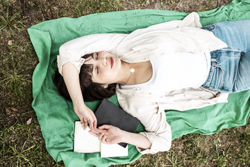 Female student sleeping with books in park. Top view of beautiful young woman lying on meadow with books and textbooks during daytime. Education concept