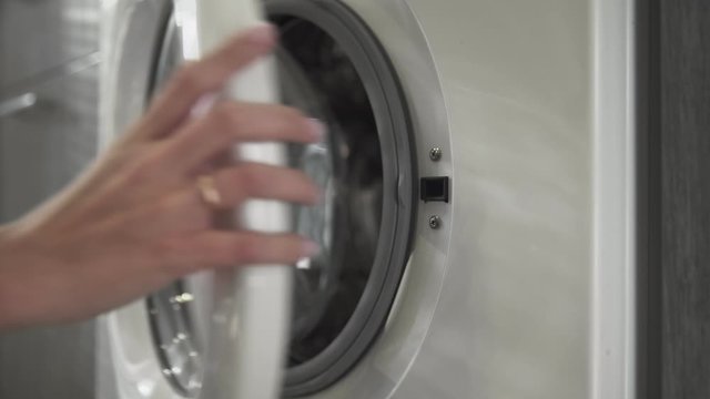 Female hand with married ring takes WHITE CLOTHES from laundry machine. Loading washing machine. Load clothes to washer machine. Load clothes laundry washing machine. Preparing laundry washing