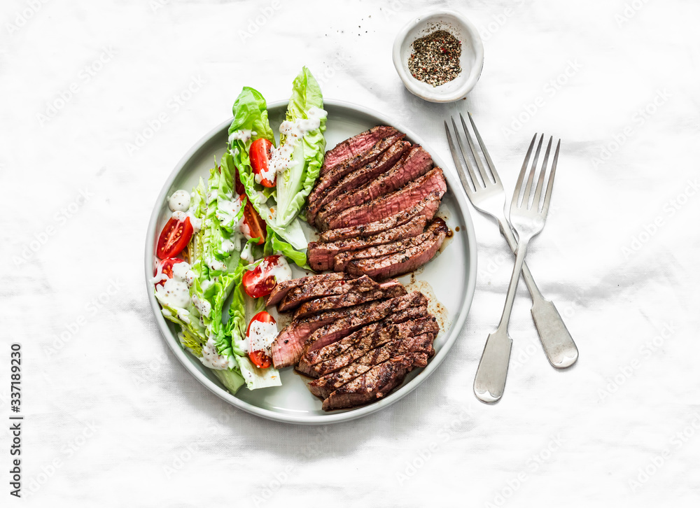 Wall mural medium rare beef steak and romaine cherry tomatoes yogurt dressing salad on a light background, top 