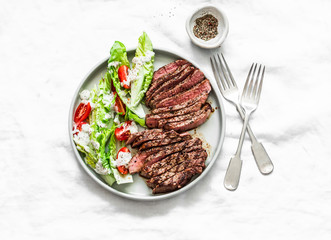 Medium rare beef steak and romaine cherry tomatoes yogurt dressing salad on a light background, top...