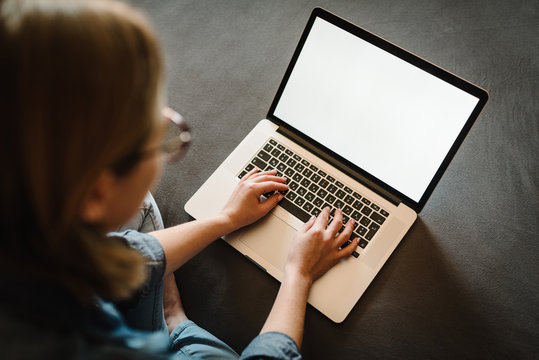 Beautiful happy young woman working and using white blank screen laptop computer in the bedroom. Freelancer. Writing, typing. Girl in social apps. Communication and technology concept. Top view.