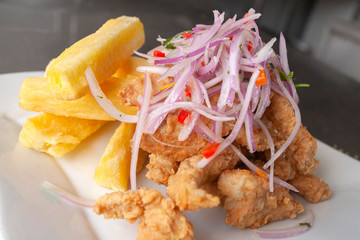 Peruvian food: chicharron de pescado or fish cracklings with fried cassava and onion salad with chili, served on a white plate