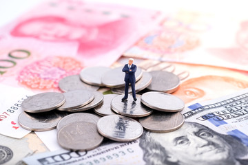 Miniature people : Businessmam standing on the coin and banknote (US dollar, Singapore dollar and Chinese Renminbi) with banknote background under sunlight. Money, business and finance concept.