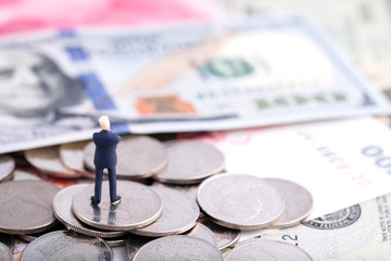Miniature people : Businessmam standing on the coin and banknote (US dollar, Singapore dollar) with banknote background under sunlight and look at money. Money, business and finance concept