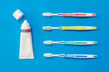 Four silicone-bristled toothbrushes and a tube of toothpaste on a blue background. Concept of oral hygiene in the family.