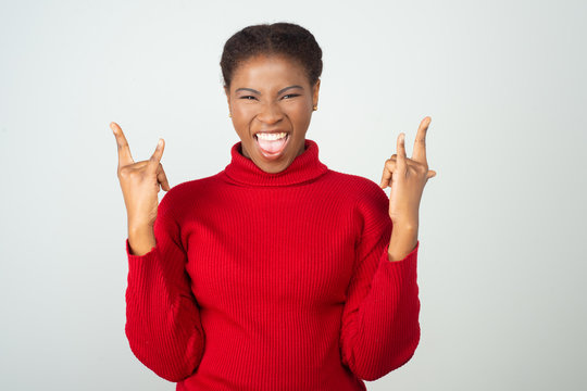 Joyful excited rock fan shouting and showing devils horn hand gesture. Beautiful young African American lady standing isolated over white background. Gestures concept