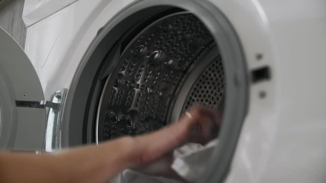 Female hand with married ring puts WHITE CLOTHES from laundry machine. Loading washing machine. Load clothes to washer machine. Load clothes laundry washing machine. Preparing laundry washing