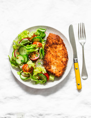 Chicken milanese and fresh romaine salad, cherry tomatoes, radishes, cucumbers salad - delicious lunch on a light background, top view