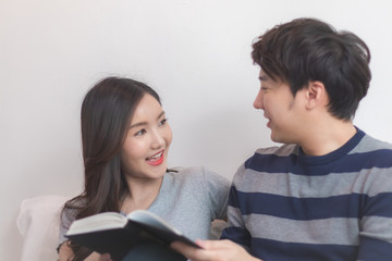 Lovely attractive young Asian couple man and woman with happy smile and reading book in romantic moment. Warm heart marriage and lover bonding and relationship. Husband and wife in love photo concept