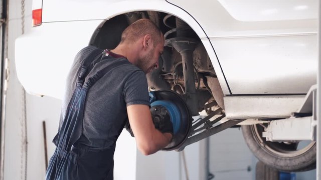 Man repairs white car. Machine is without wheels. Worker is fixing car in service center.