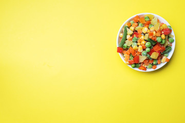 Chopped frozen vegetables in a plate on a yellow background. Corn peas pepper carrots. copy space.