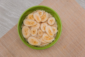 Oatmeal with banana slices in a green cup on a white wooden table. Healthy eating Diet for gastritis