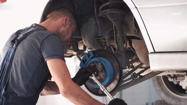 Man repairs white car. Machine is without wheels. Worker is fixing car in service center.