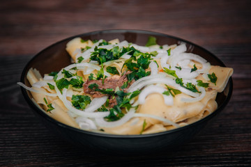 Beshbarmak in a dark plate, on a light wooden table. Dish of pastry with meat. Eastern cuisine