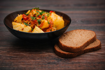 Stewed potatoes with cabbage in a dark plate on a brown wooden table. Rustic cuisine.