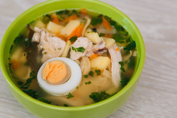 Green plate with noodle soup and half an egg on a light wooden table. Diet soup. Healthy eating