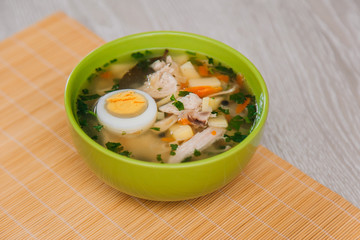 Green plate with noodle soup and half an egg on a light wooden table. Diet soup. Healthy eating
