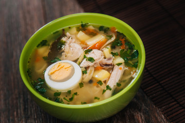 Green plate with noodle soup and half an egg on a dark wooden table. Diet soup. Healthy eating