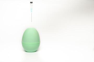 Hand holding a syringe with needle injecting a green egg model isolated on white background. Concept of medical vaccination for Covid-19 pandemic.