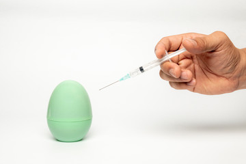 Hand holding a syringe with needle injecting a green egg model isolated on white background. Concept of medical vaccination for Covid-19 pandemic.