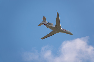  small white jet airplane flies in the blue almost cloudless sky