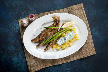 Fried smelt served on a white plate with potatoes, sauce and onions