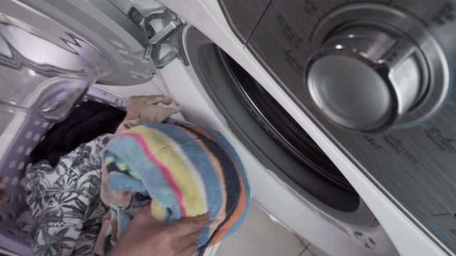 Close up of a woman in homely clothes sitting in Front of a washing Machine. She Loads the washer with dirty laundry, Top view
