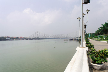 Howrah bridge landscape scene on Hooghly river horizon over water. Photography from millenium garden park promade area on the Ganges riverbank. Kolkata waterfront cityscape. West Bengal India Asia