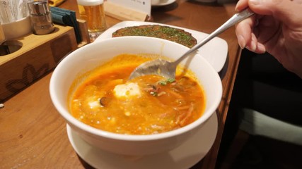 Close up female hand adding sour cream to borsch soup on spoon. Woman stirring solyanka cream soup hodgepodge at table in home kitchen