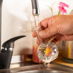 A man pours tap water into a glass flask.