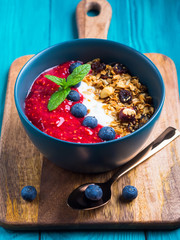 Yogurt smoothie bowl with blended raspberries, blueberries and oat matcha granola on dark green wooden background. Delicious healthy breakfast concept